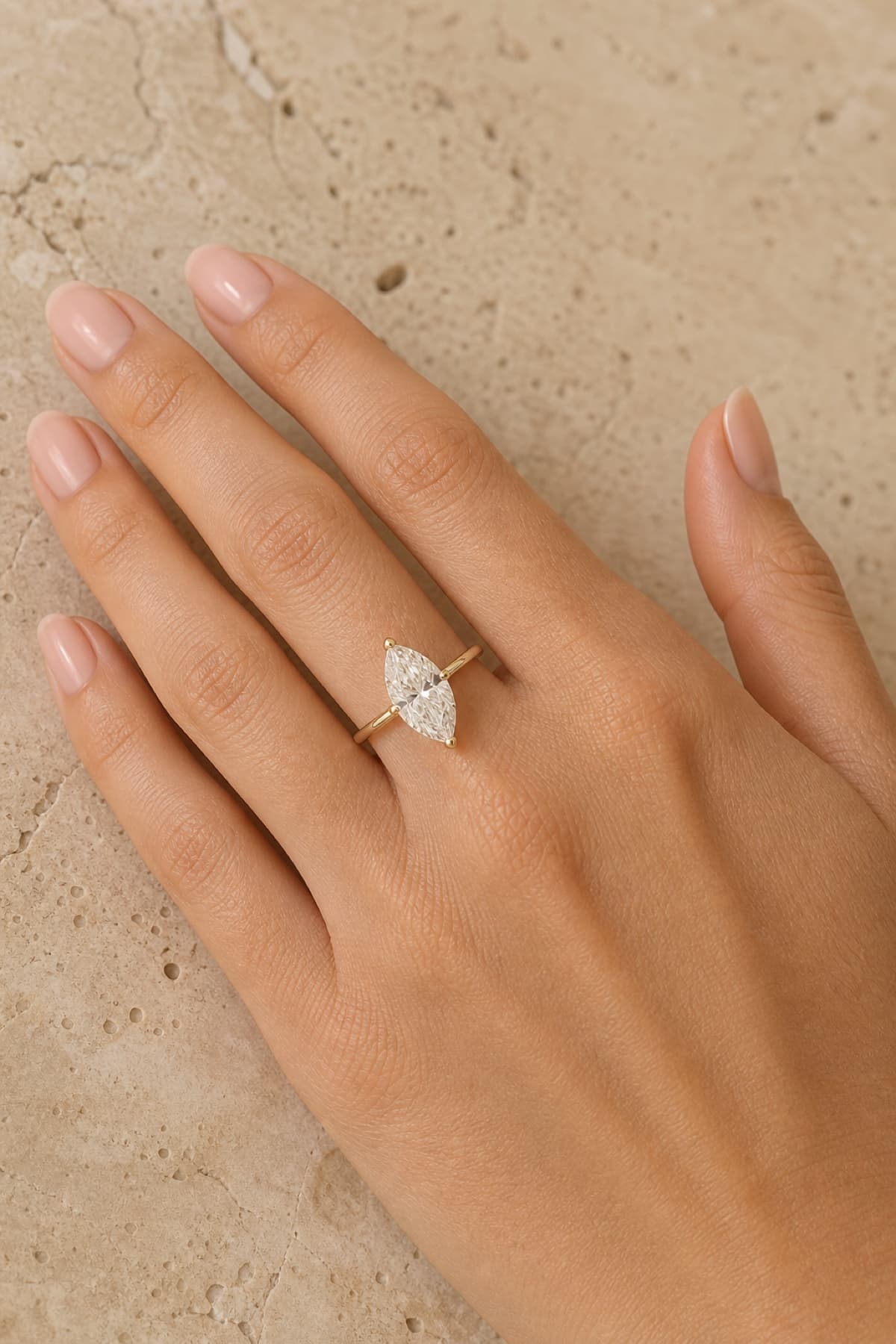 Marquise engagement ring on a woman's left hand ring finger against a clean travertine studio surface