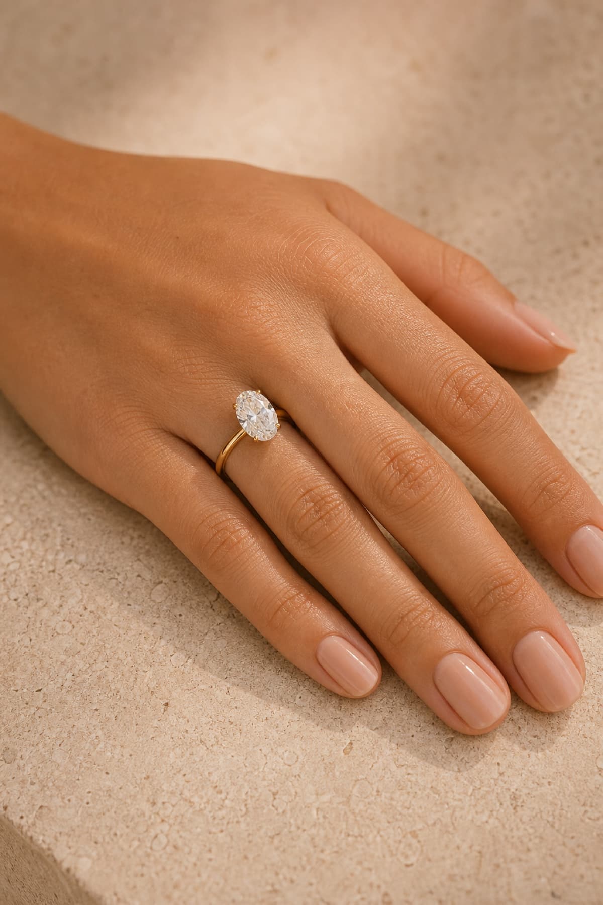Oval solitaire engagement ring on a woman's left hand ring finger in a warm jeweler's studio